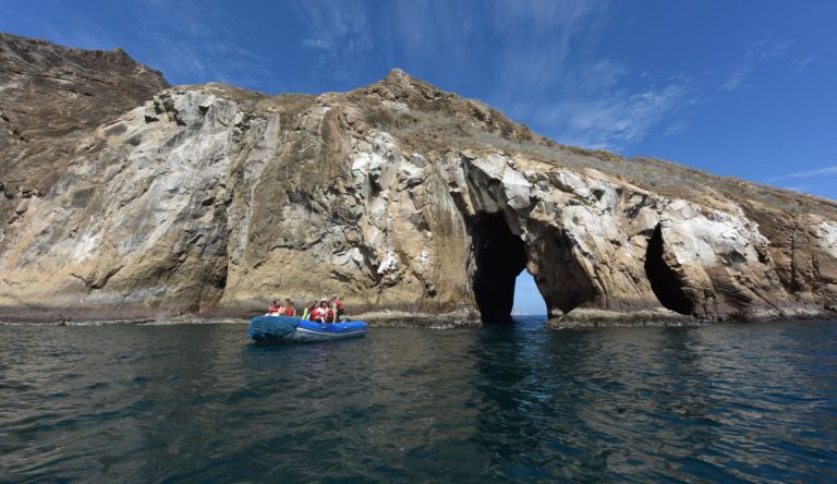 Cerro Brujo - San Cristobal in Galapagos Islands, rock formations with Kicker rock at background and tourist in panga