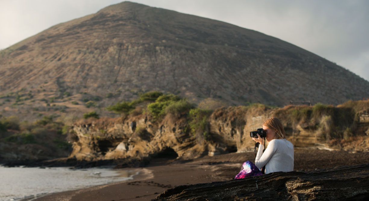 Egas Port in Santiago Island wit rocky beach and tourist taking pictures, background of volcano